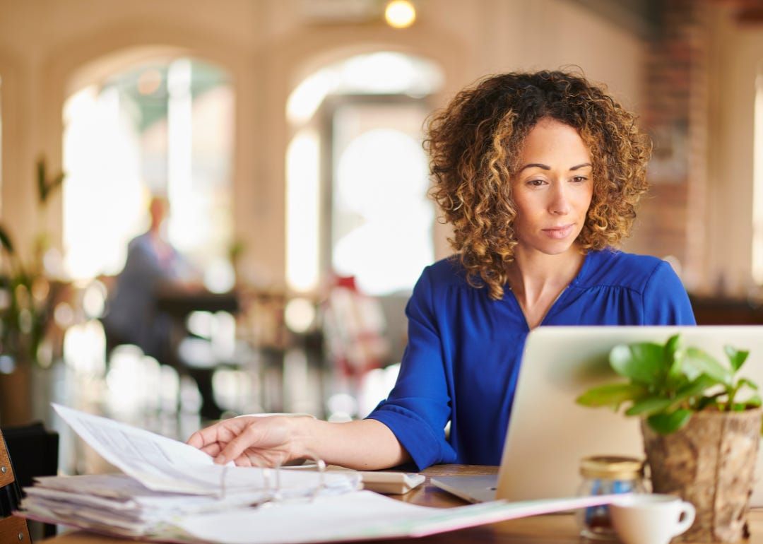 A person with a binder of papers and a computer working at a table.